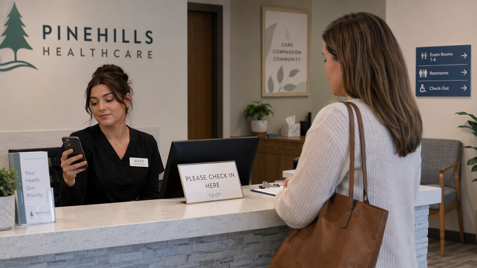 Clinic receptionist glancing at phone notification while patient checks in at front desk